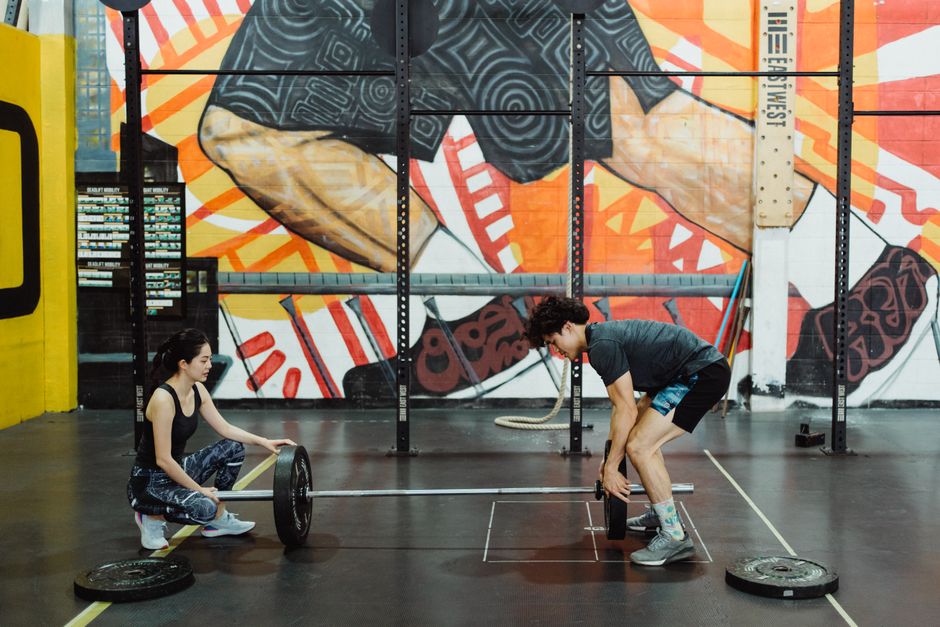 A young personal trainer helping an individual with strength training in a gym setting.