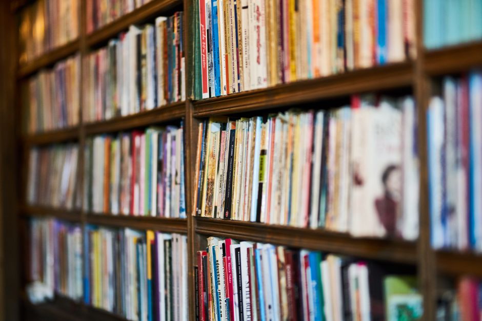 A cozy bookshelf featuring a diverse collection of books, teapots, and signage.